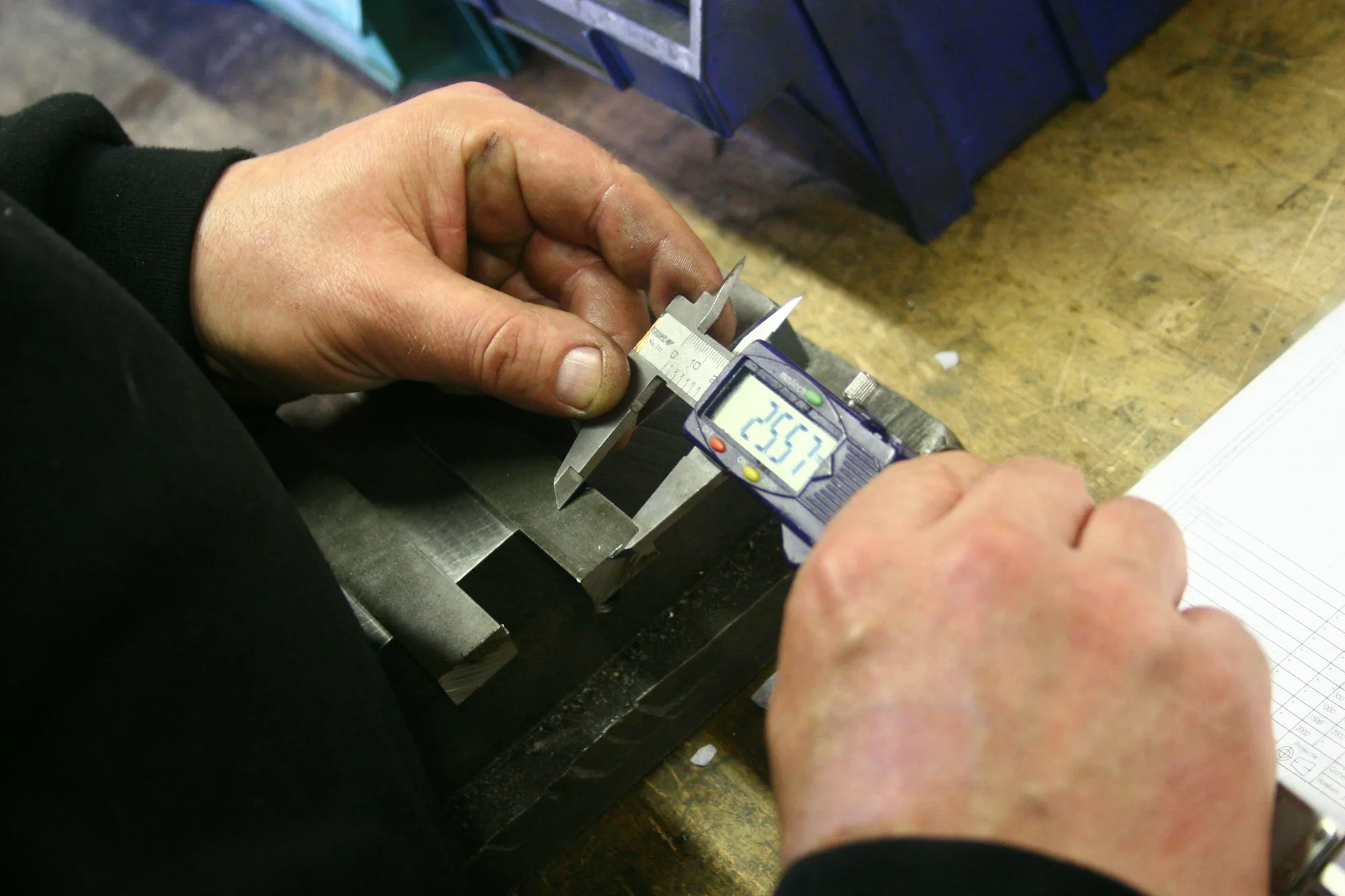 Hands using a digital caliper to measure a metal component at a workbench