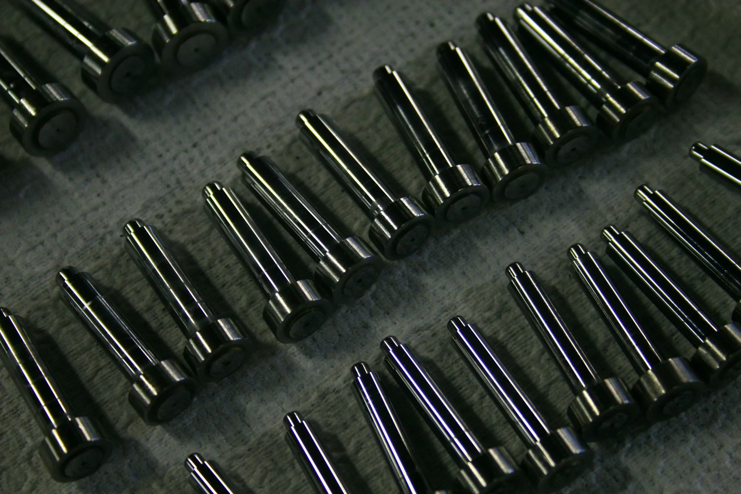 Rows of polished cylindrical metal components arranged on a workshop surface